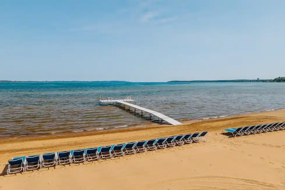 Aerial view of the beach with a dock and blue lounge chairs under a wide sky