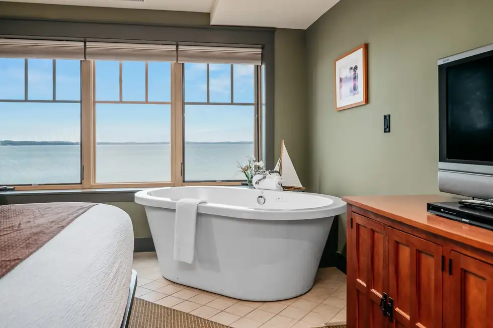 Soaker tub in front of bay windows, with a TV on the wall