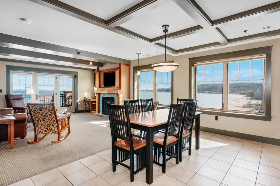 Suite dining table under a coffered ceiling, bay windows looking out over the water