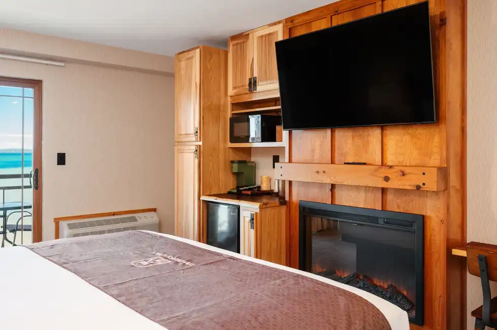 Bed facing an electric fireplace and a flat-screen TV